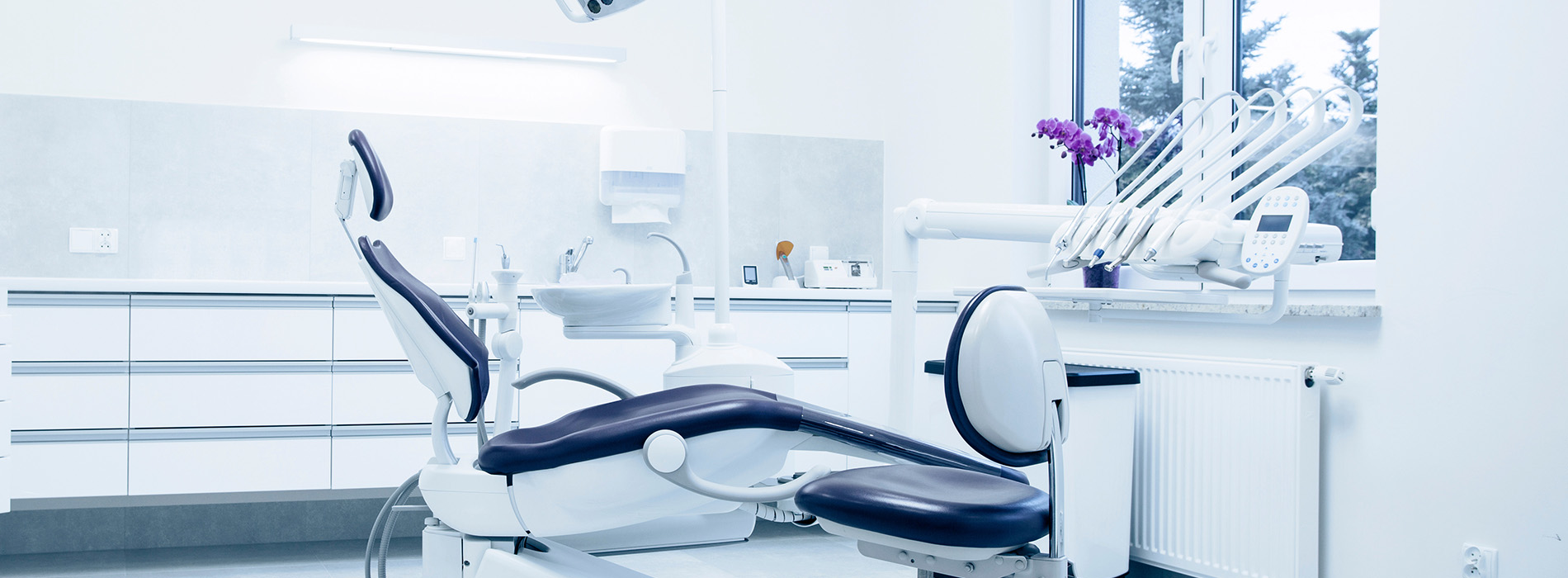 The image shows a modern dental clinic interior with various pieces of equipment, including a dental chair and an X-ray machine.