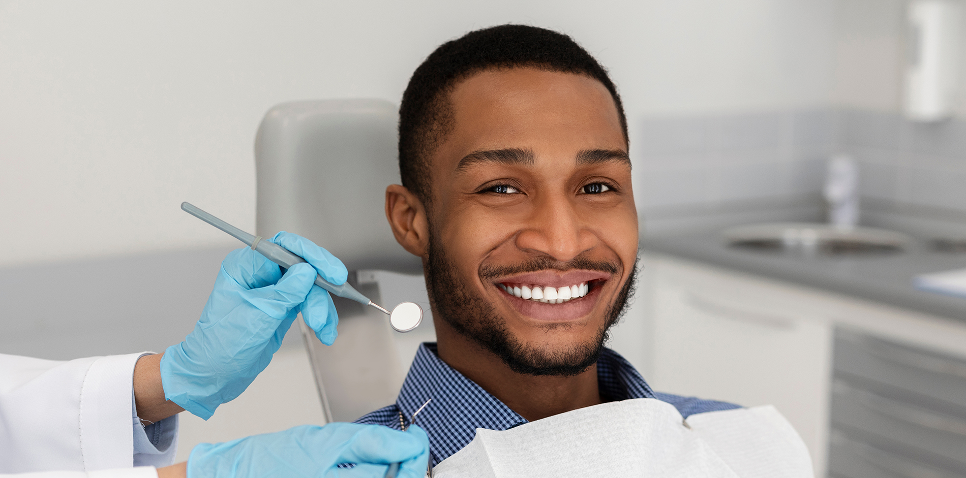 A person is seated in a dental chair, receiving care from a dental professional who stands behind them.