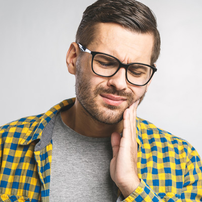 A man with a beard and glasses, holding his hand to his mouth as if in pain or discomfort.