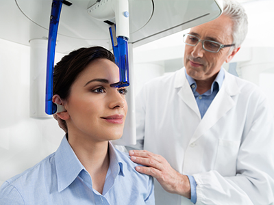 A woman in a dental chair with a blue headband, receiving a dental scan from a dentist.