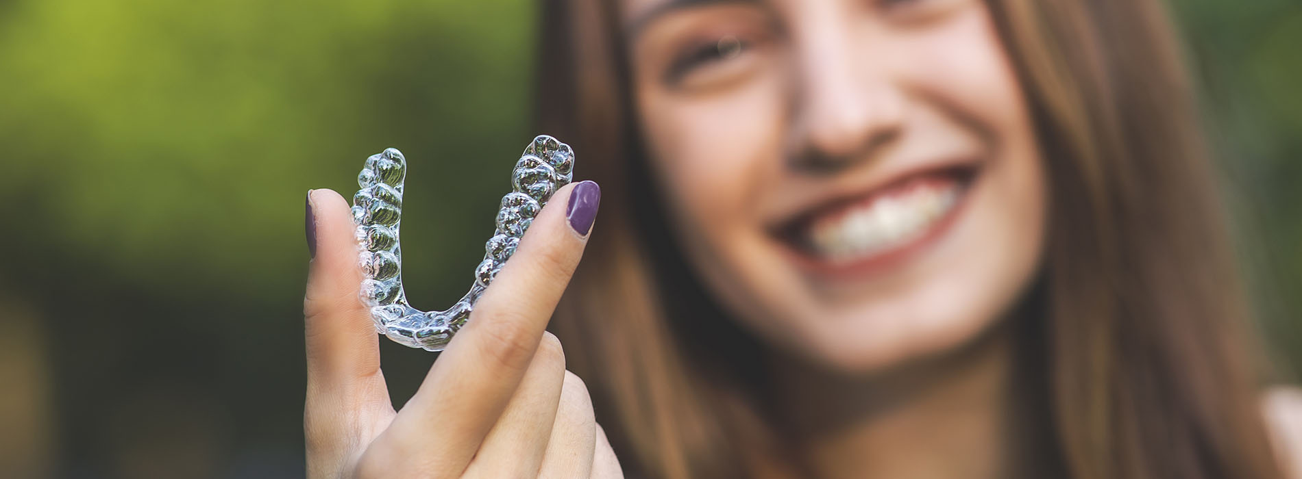 An image of a smiling woman holding up a clear, plastic dental retainer.